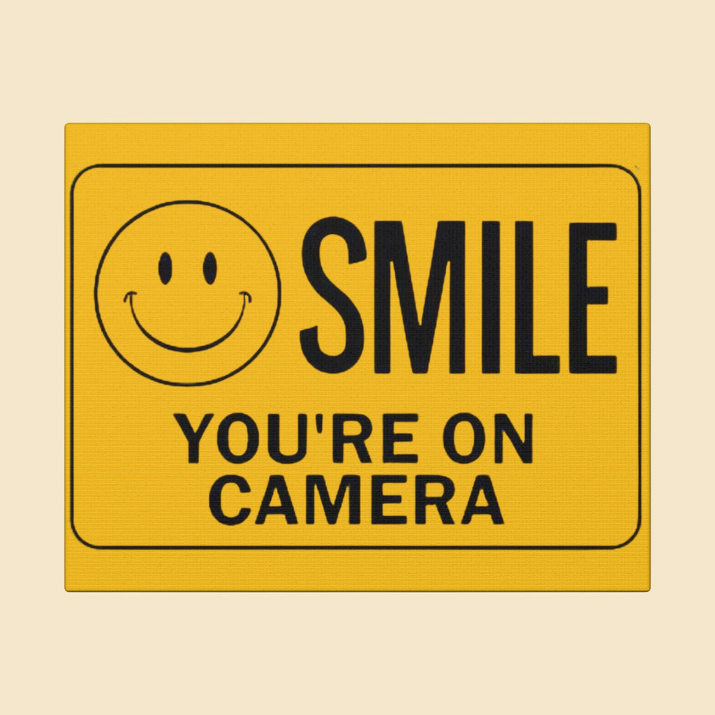 Yellow security camera sign with smiley face and text 'SMILE YOU'RE ON CAMERA' on a white background