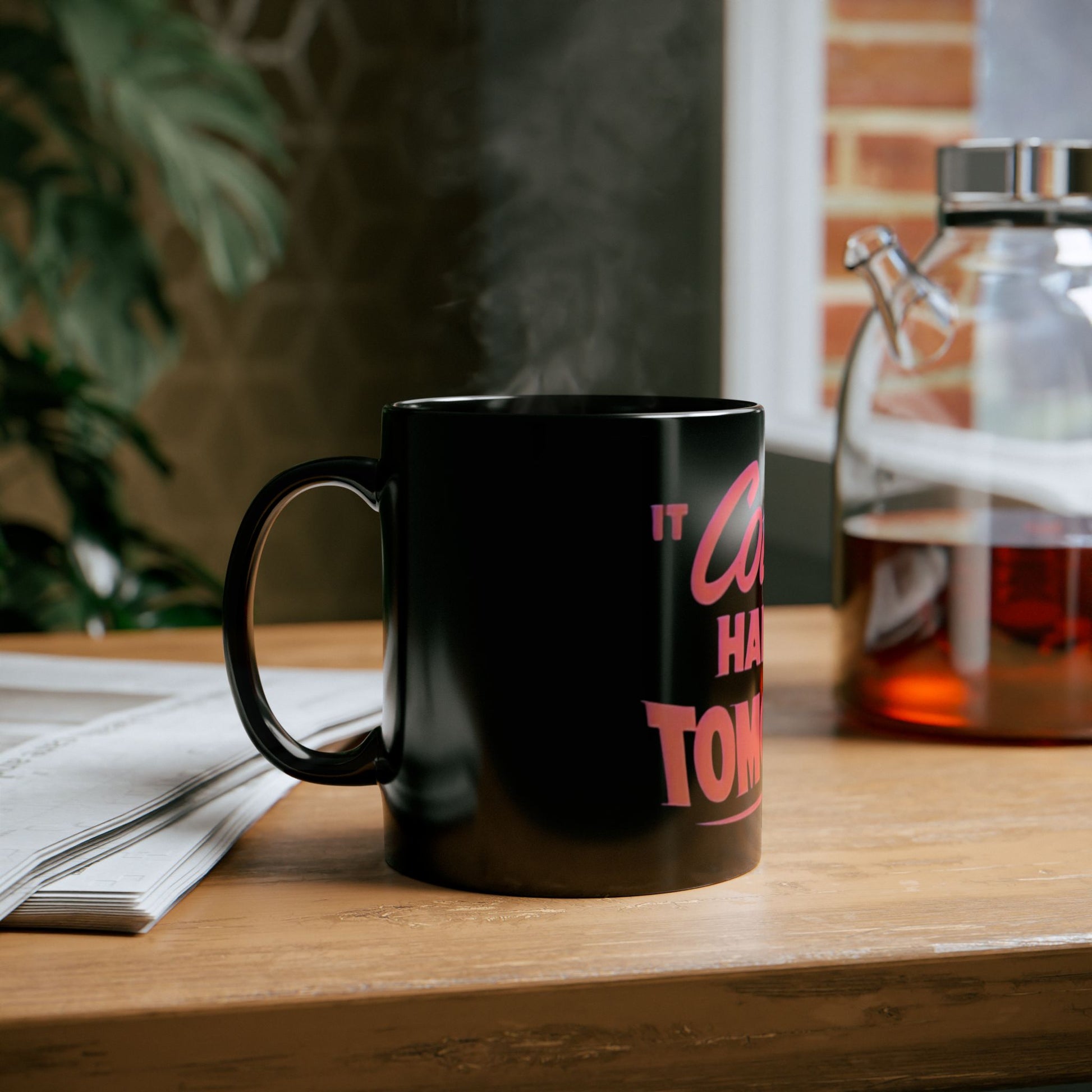 Black mug with pink text on a wooden table with a blurred background