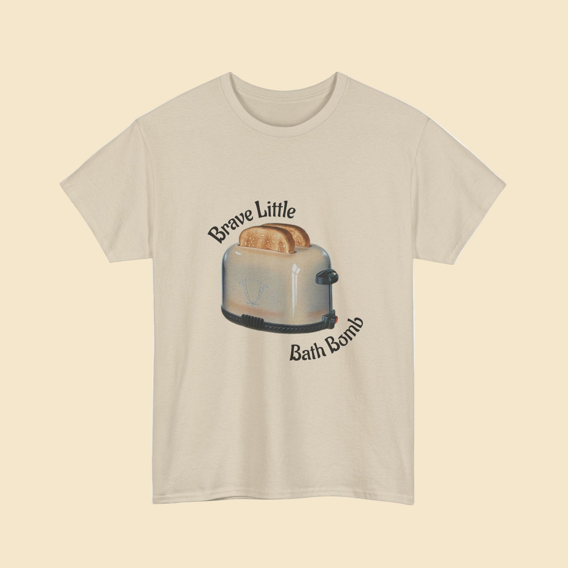 Beige t-shirt with a graphic of a toaster and text 'Brave Little Bath Bomb' on a white background