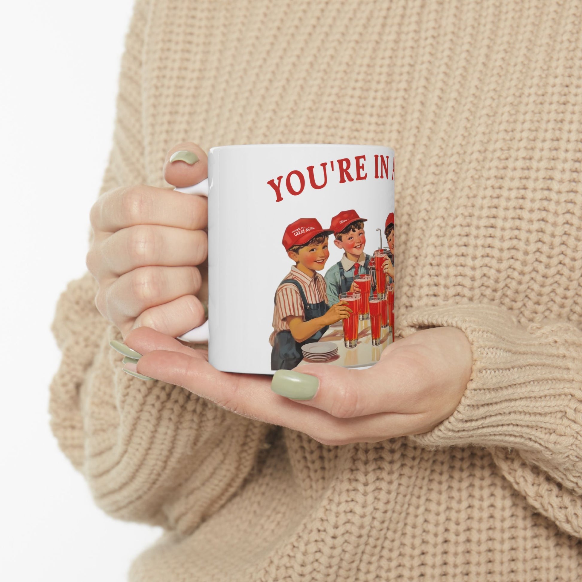 Person holding a mug with a vintage-style illustration and text 'YOU'RE IN' on a beige background