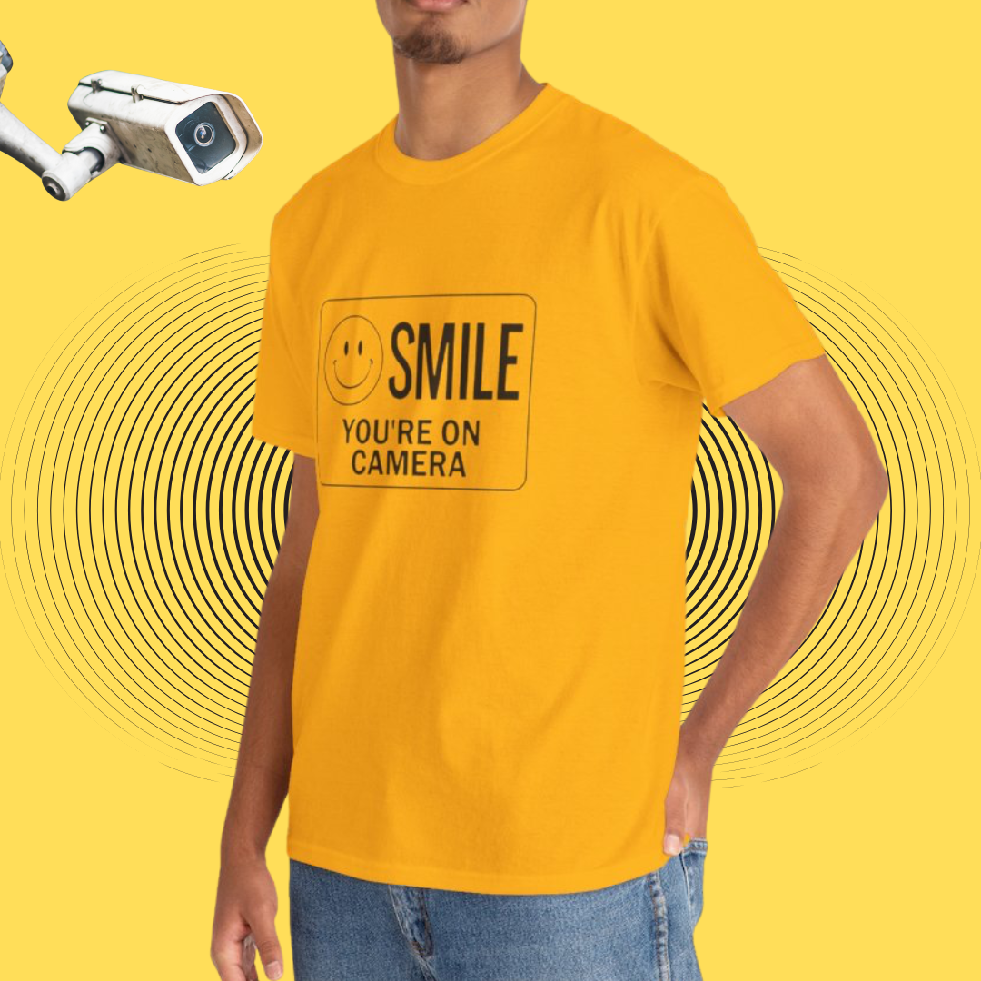 Person wearing a yellow t-shirt with 'SMILE YOU'RE ON CAMERA' text and smiley face on a yellow background.