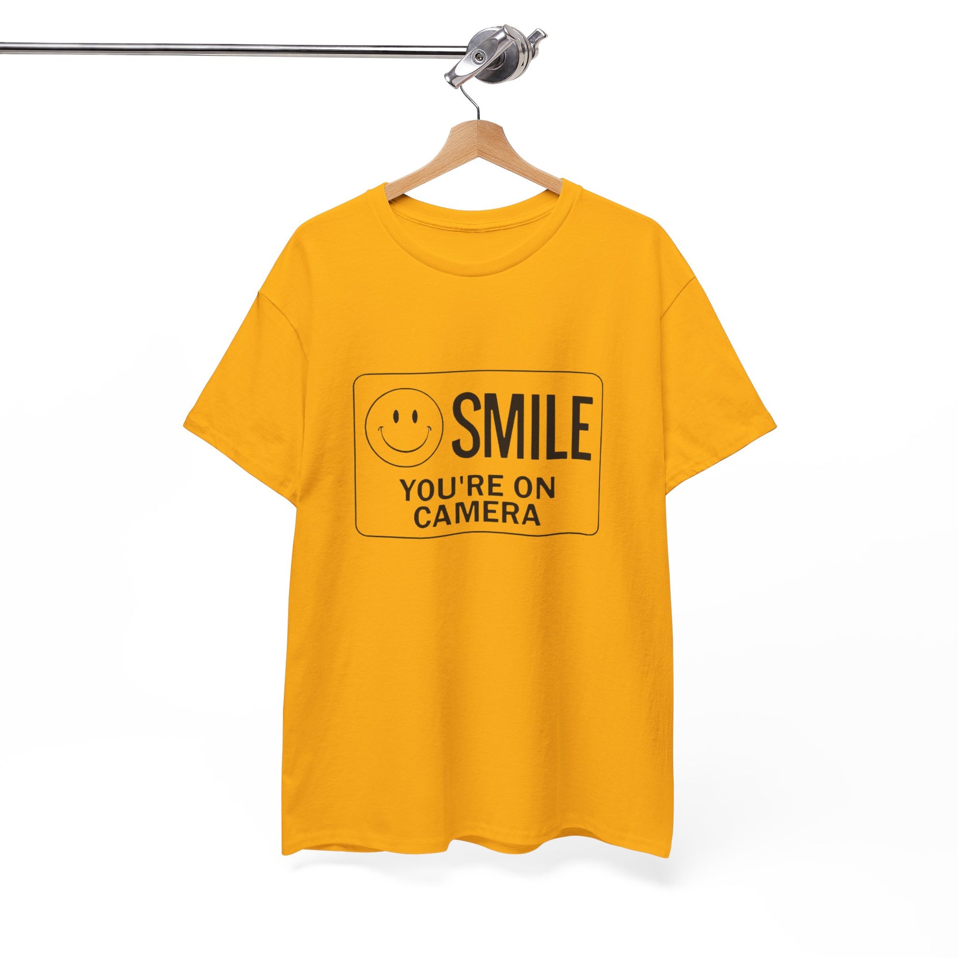 Yellow t-shirt with 'SMILE YOU'RE ON CAMERA' text on a hanger against a white background